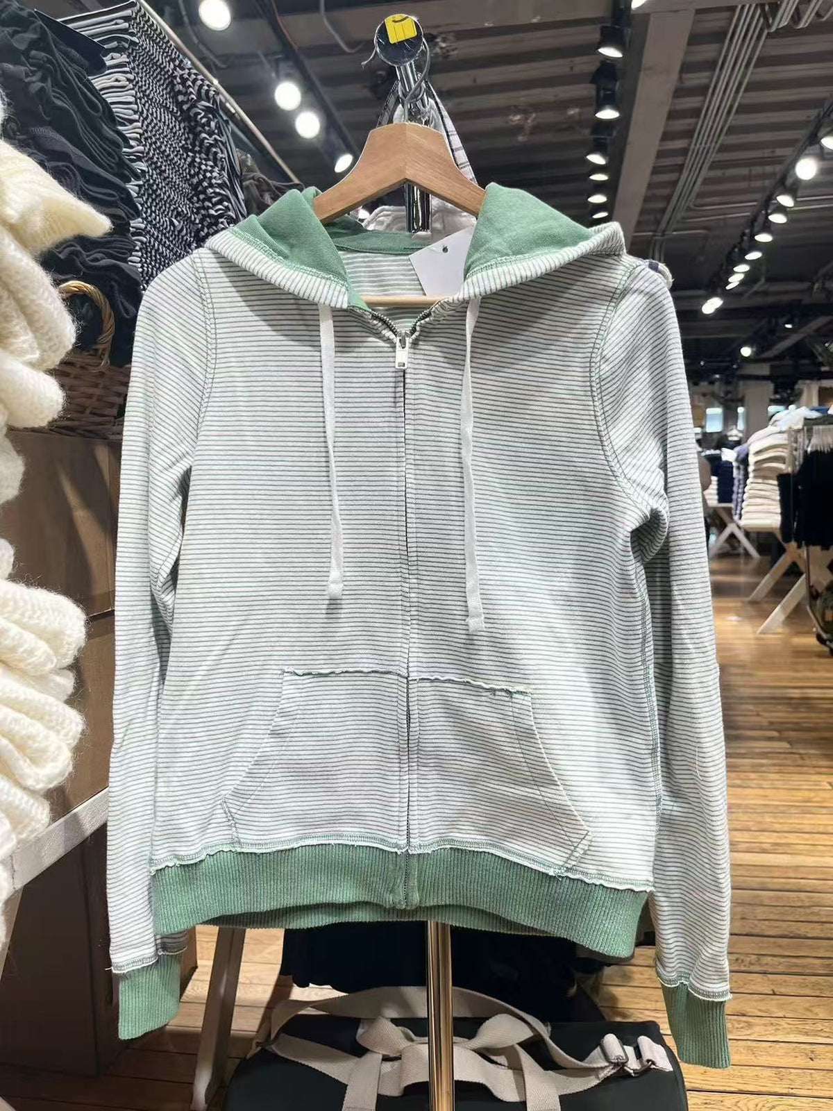 Green striped zip-up hoodie on a hanger showing the front pocket, drawstrings and green ribbed hem