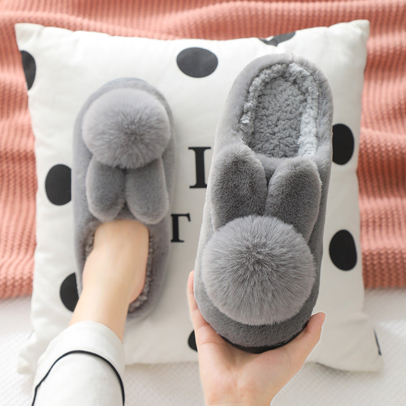 Gray plush bunny slippers, one worn on a foot and one held to show the thick sole, gray variant