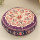 Round cushion with a purple mandala print top in pink and cream and a dark floral border, on a beige rug