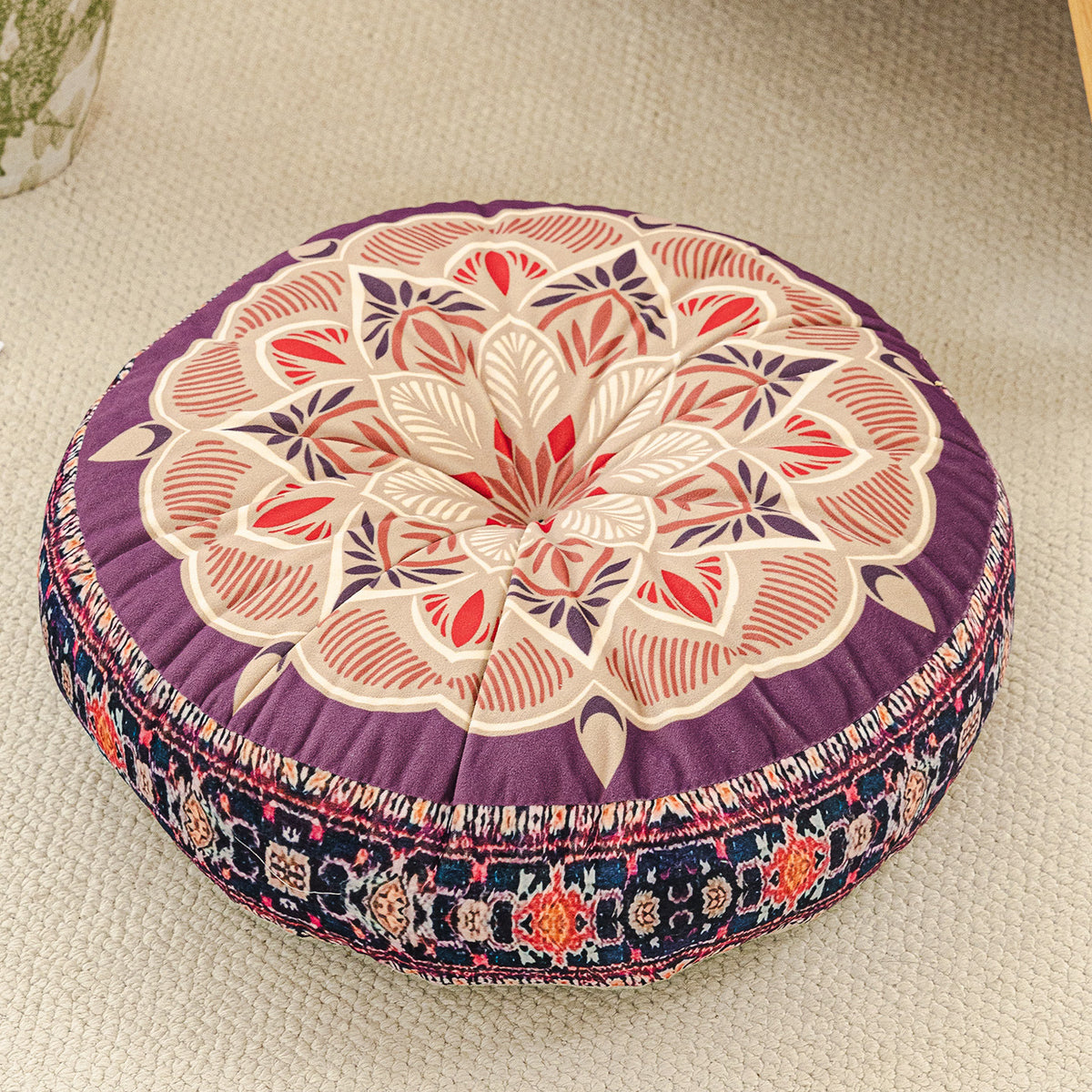 Round cushion with a purple mandala print top in pink and cream and a dark floral border, on a beige rug