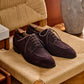 Dark brown suede lace-up derbys with wooden trees, shown on a rush chair in warm indoor light