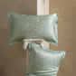 Pair of green bamboo leaf jacquard silk pillowcases, one lying flat and one propped on a column