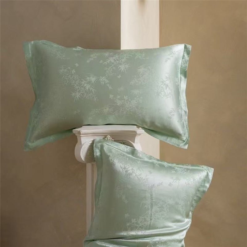 Pair of green bamboo leaf jacquard silk pillowcases, one lying flat and one propped on a column