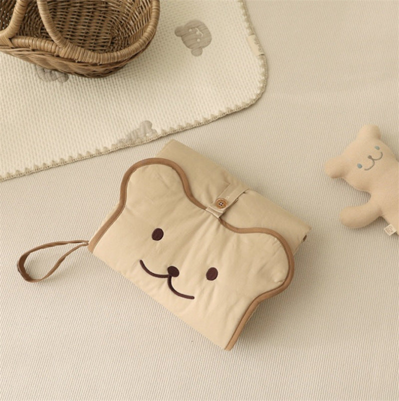 Folded cotton baby changing pad held in hand showing its compact notebook size