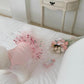 Small white dog wearing the pink cherry print tulle dog dress, seen from behind on a bed