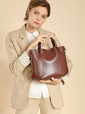 Woman holding a chestnut brown cowhide leather bucket tote by its top handles, wearing a beige blazer