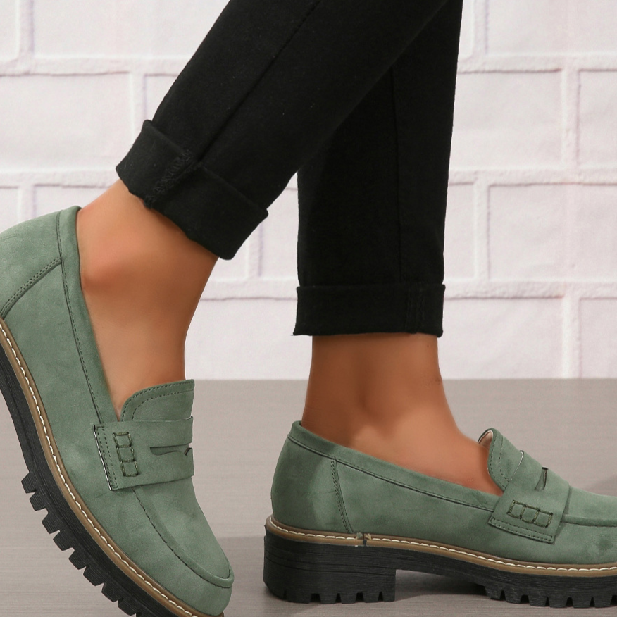 Green penny loafer with saddle strap and lug sole worn with black cuffed trousers