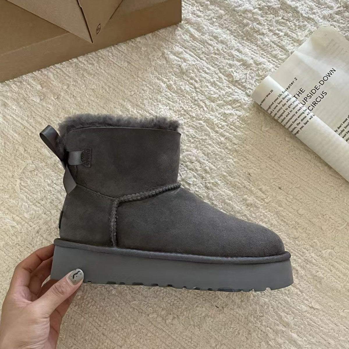 Hand holding a gray suede platform ankle boot with a back bow, side view of the thick EVA sole