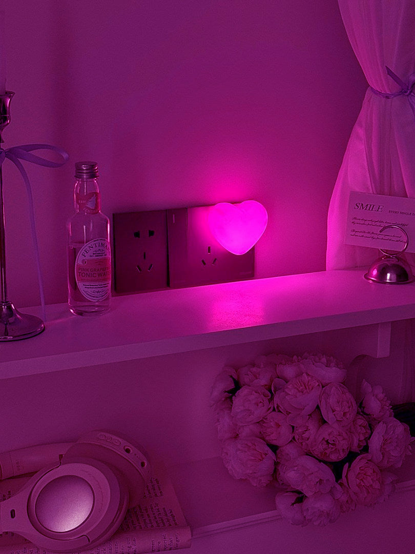 Pink heart night light casting a soft glow across a dim bedroom shelf