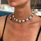 Cowrie shell choker on black cord worn at the throat, knots visible between the shells