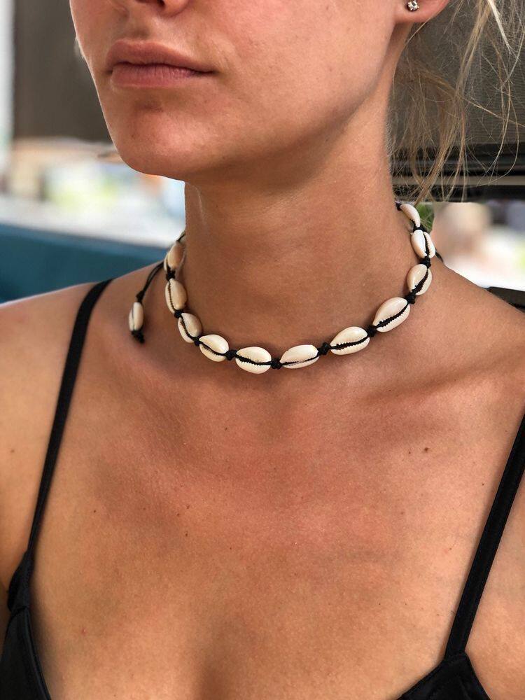 Cowrie shell choker on black cord worn at the throat, knots visible between the shells