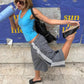 Woman in gray striped wide-leg pants lifting one leg in a dance pose, blue tank top and sunglasses