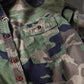 Men's washed camouflage long sleeve button shirt with two flap chest pockets detail of the red front buttons on camo