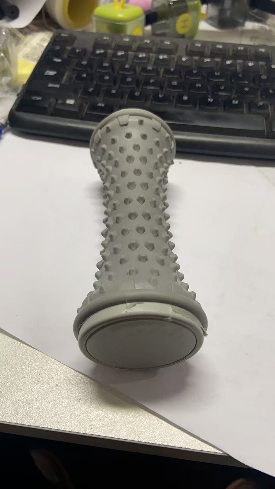 Grey nubbed foot roller standing upright on a desk beside a keyboard
