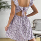 Floral square neck mini dress showing the open back that ties with a bow, standing outdoors