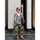 Woman in sunglasses wearing green camouflage wide-leg pants, a striped top and a black bag, three quarter view