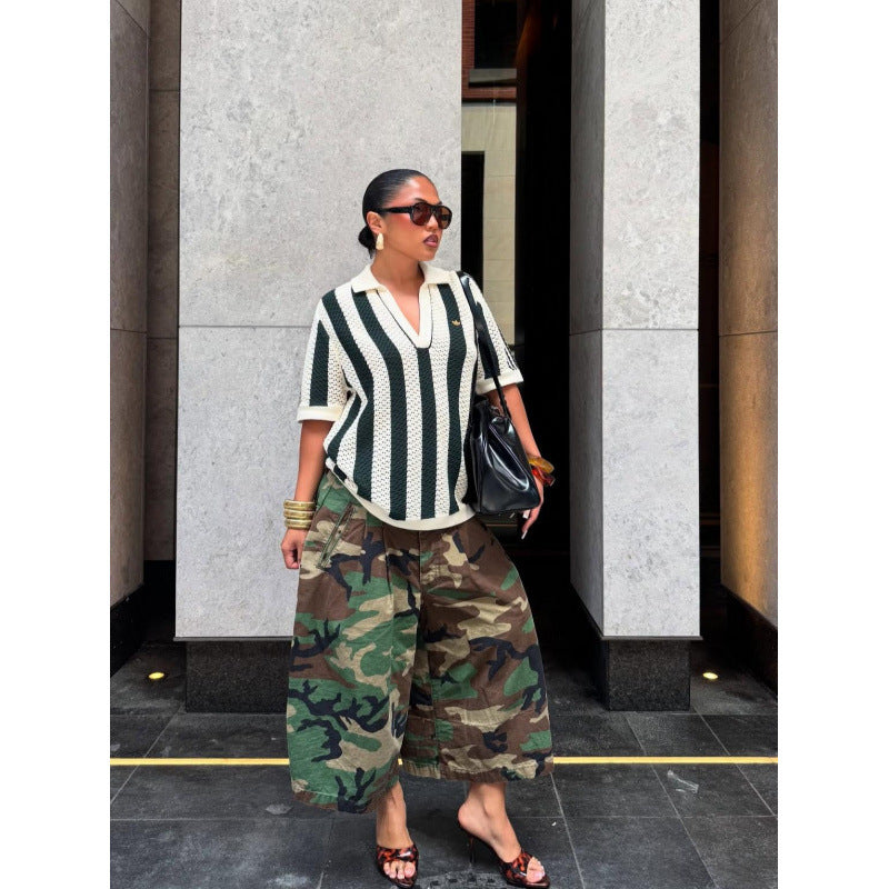 Woman in sunglasses wearing green camouflage wide-leg pants, a striped top and a black bag, three quarter view