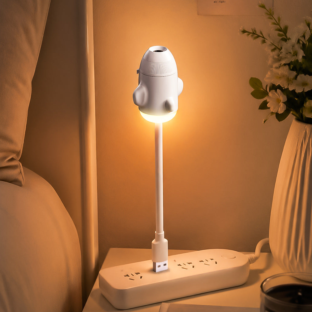 White rocket projector on its gooseneck plugged into a bedside power strip, glowing warm