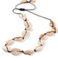 Cowrie shell choker on dark cord photographed at an angle, each shell knotted between two hitches