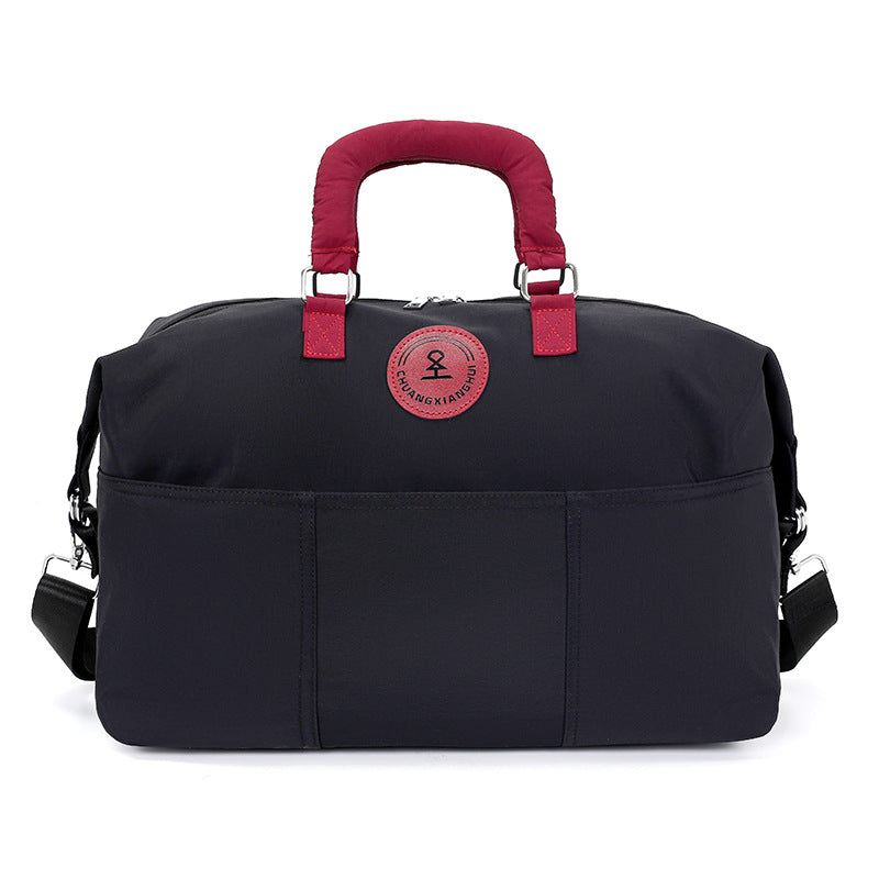Black duffel travel bag with burgundy padded handles, round patch and front slip pockets, second view