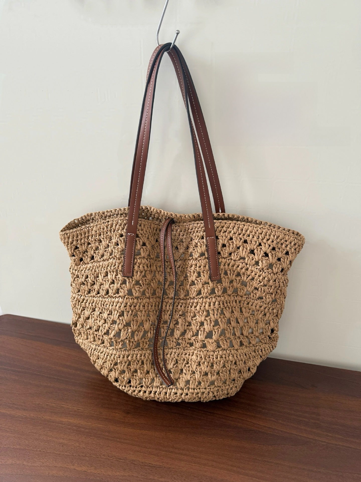 Side profile of the woven straw tote showing its roomy depth and natural khaki straw weave