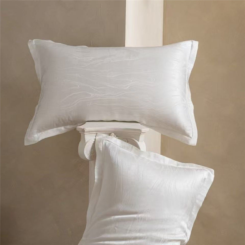 Pair of ivory wave pattern jacquard silk pillowcases, one lying flat and one propped on a column