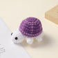 Crocheted purple shell white turtle, handmade wool charm on a cream surface