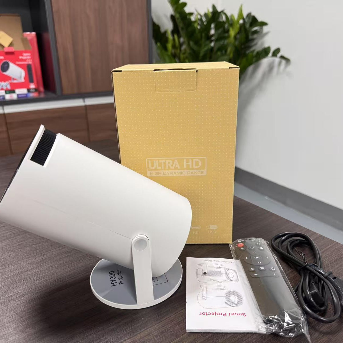 White projector on its base beside the retail box marked Ultra HD, remote control, power cord and manual