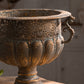 Close up of the pierced floral medallion band and lobed bowl of an aged bronze iron urn with scroll handle