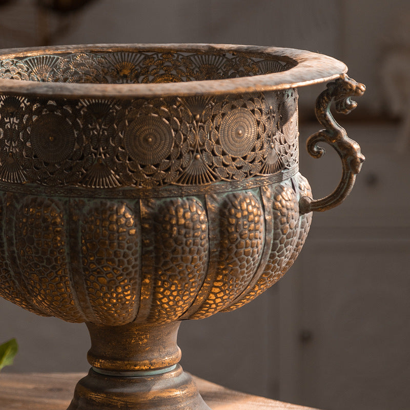 Close up of the pierced floral medallion band and lobed bowl of an aged bronze iron urn with scroll handle