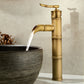 Tall antique copper bamboo faucet with a curved neck pouring water into a grey stone vessel bowl