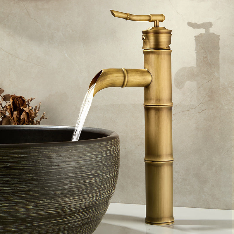 Tall antique copper bamboo faucet with a curved neck pouring water into a grey stone vessel bowl