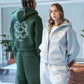 Gray option photo of a gray zip hoodie front beside a green hoodie with a clover back motif, size XXXL