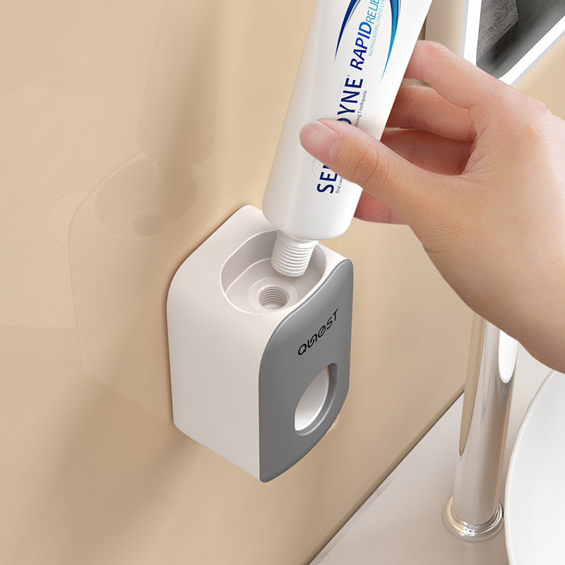 Hand sliding a standard toothpaste tube into the top socket of the wall mounted gray toothpaste dispenser