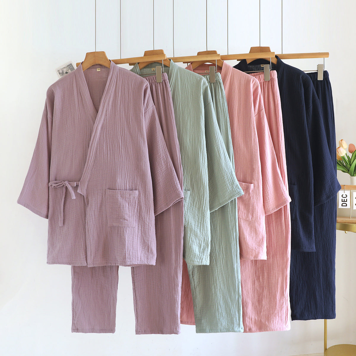 Four kimono style cotton gauze pajama sets hanging on wooden hangers in purple, green, pink and navy