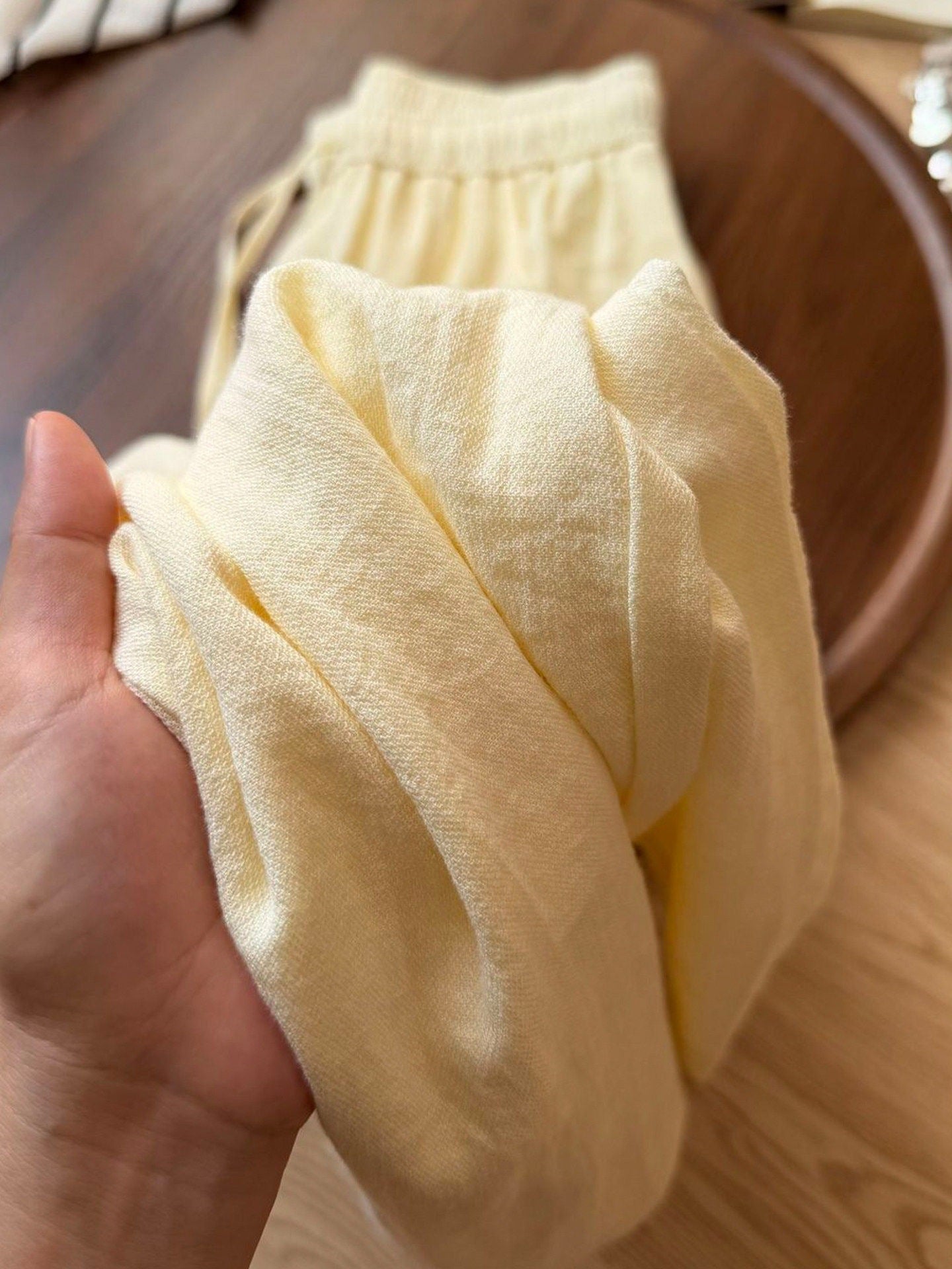 Pale yellow cotton linen pants held to show the soft open weave texture
