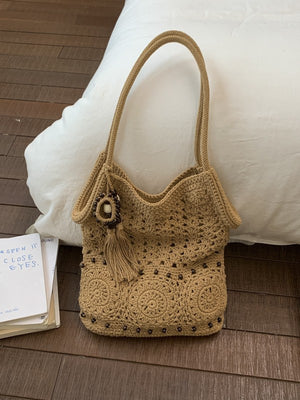 Tan crochet cotton shoulder bag with circular medallions and a wood bead tassel against a white pillow