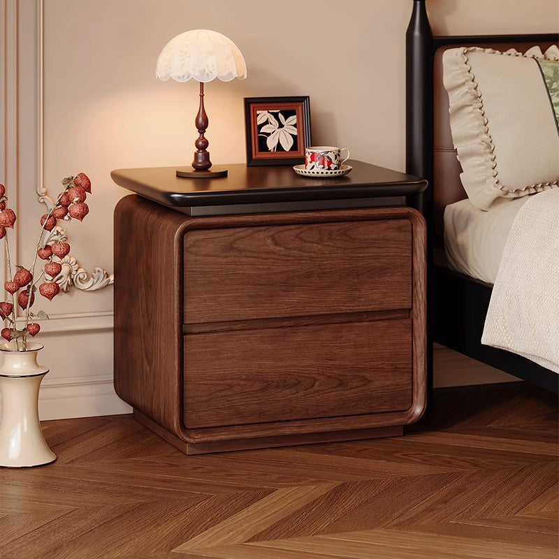 Walnut bedside table with two drawers and a black floating top beside a bed