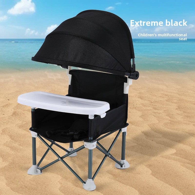 Black folding baby feeding chair with canopy and white tray photographed on sand