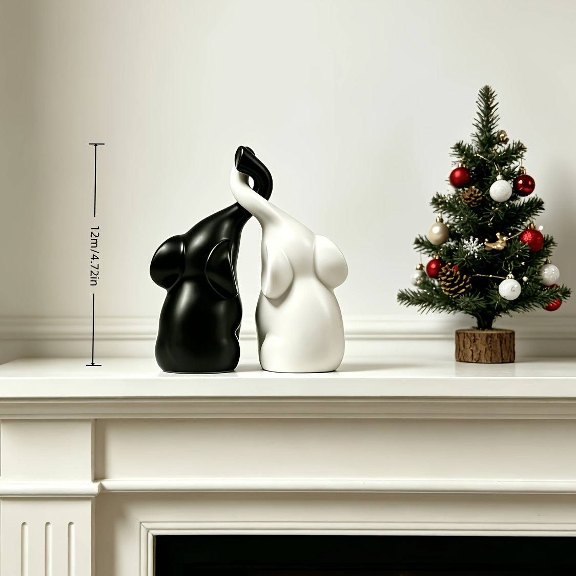 Couple elephant figurines shown about 12 cm tall on a mantel beside a small decorated tree