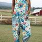 Size XL option: Aqua blue overalls with a pink and blue floral print, cuffed legs and pockets on a farm lawn
