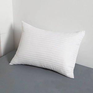 White striped bed pillow resting against a headboard on a grey fitted sheet
