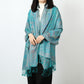 Woman wearing a teal paisley jacquard scarf over a white turtleneck with matching teal tassels