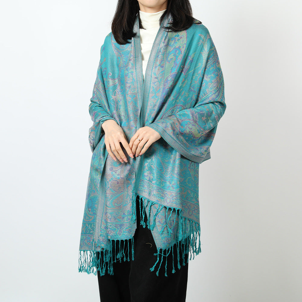 Woman wearing a teal paisley jacquard scarf over a white turtleneck with matching teal tassels