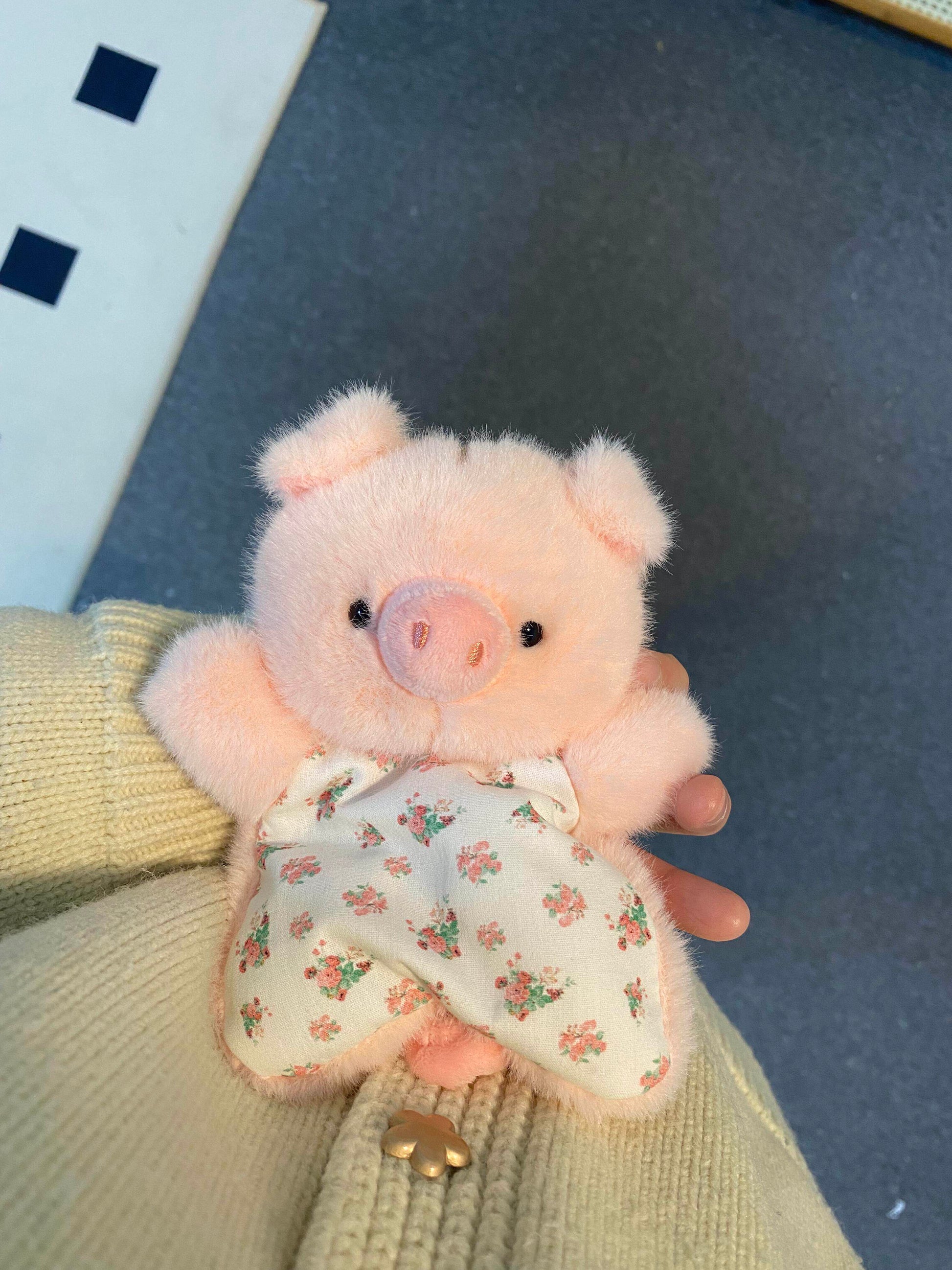 Pink plush pig squishy bean bag toy held in hand, snout face and floral cotton apron body