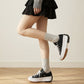 Black low-top platform canvas sneakers in two poses with a chunky white sole, worn with a black ruffle skirt