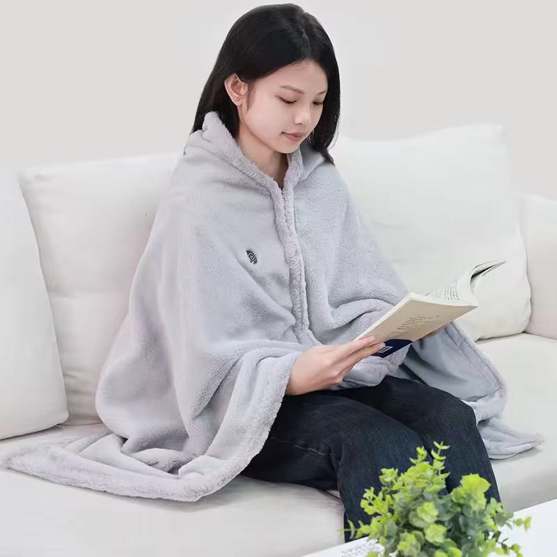 Woman in a gray plush shawl blanket reading a book on a white sofa beside a green plant