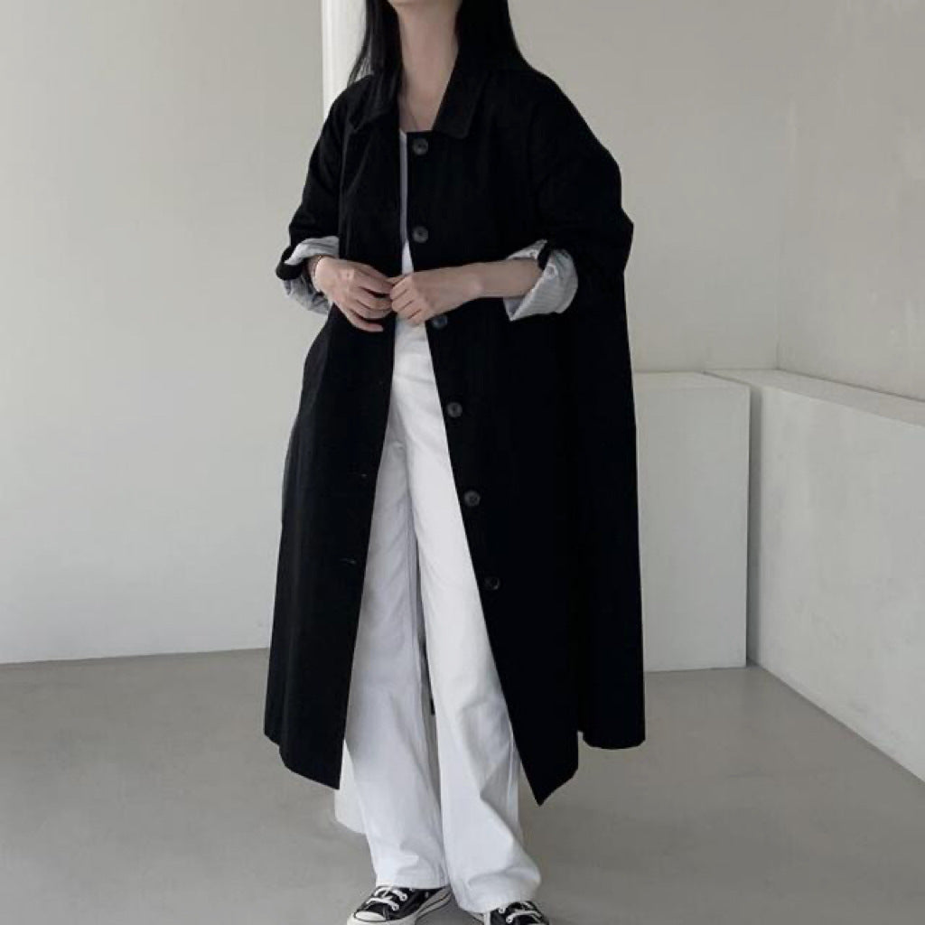 Black single breasted long trench coat with lapel collar worn open over white trousers