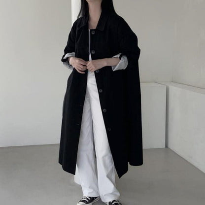 Black single breasted long trench coat with lapel collar worn open over white trousers