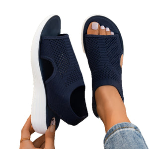 Navy open toe knit slingback wedge sandals, one held up and one worn, white midsole and side keyhole
